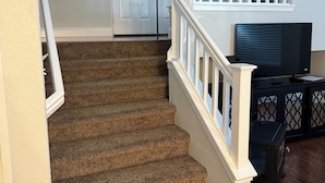 A staircase with carpeted steps, white railings, and a landing area with a television and storage unit. - Spacious Waterfront Home for Groups (Stockton)