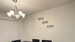 A dining room with a dark wooden table and six chairs, a chandelier, and wall decorations with words like "eat," "love," and "drink." - Spacious Waterfront Home for Groups (Stockton)