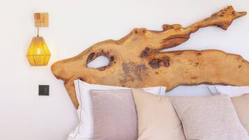 Una cama con dos almohadas, una lámpara fijada a la pared y un cabecero grande de madera.