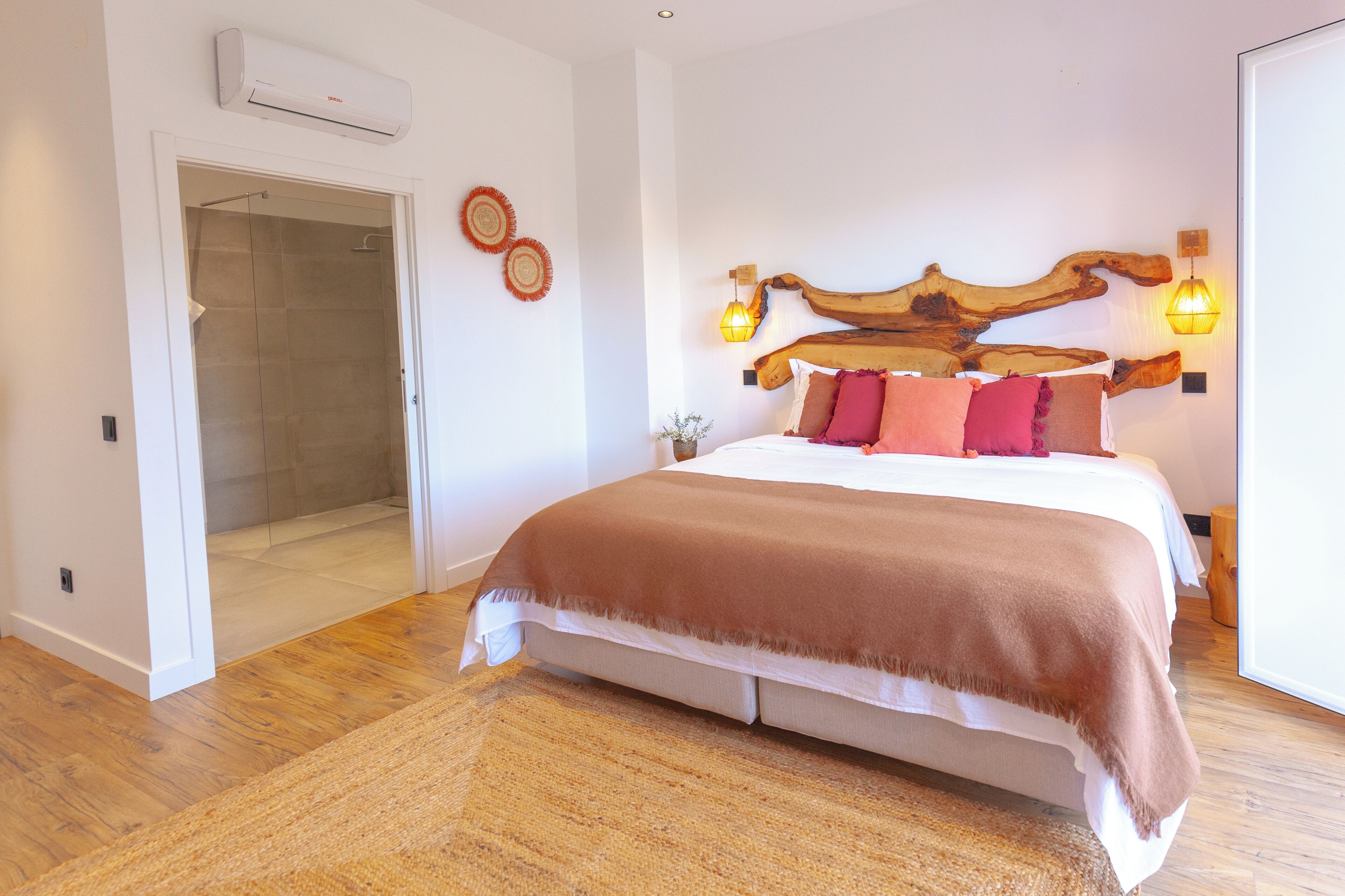 A bedroom with a wooden headboard, a large bed with a brown blanket, two wall-mounted lights, and a glass shower door.