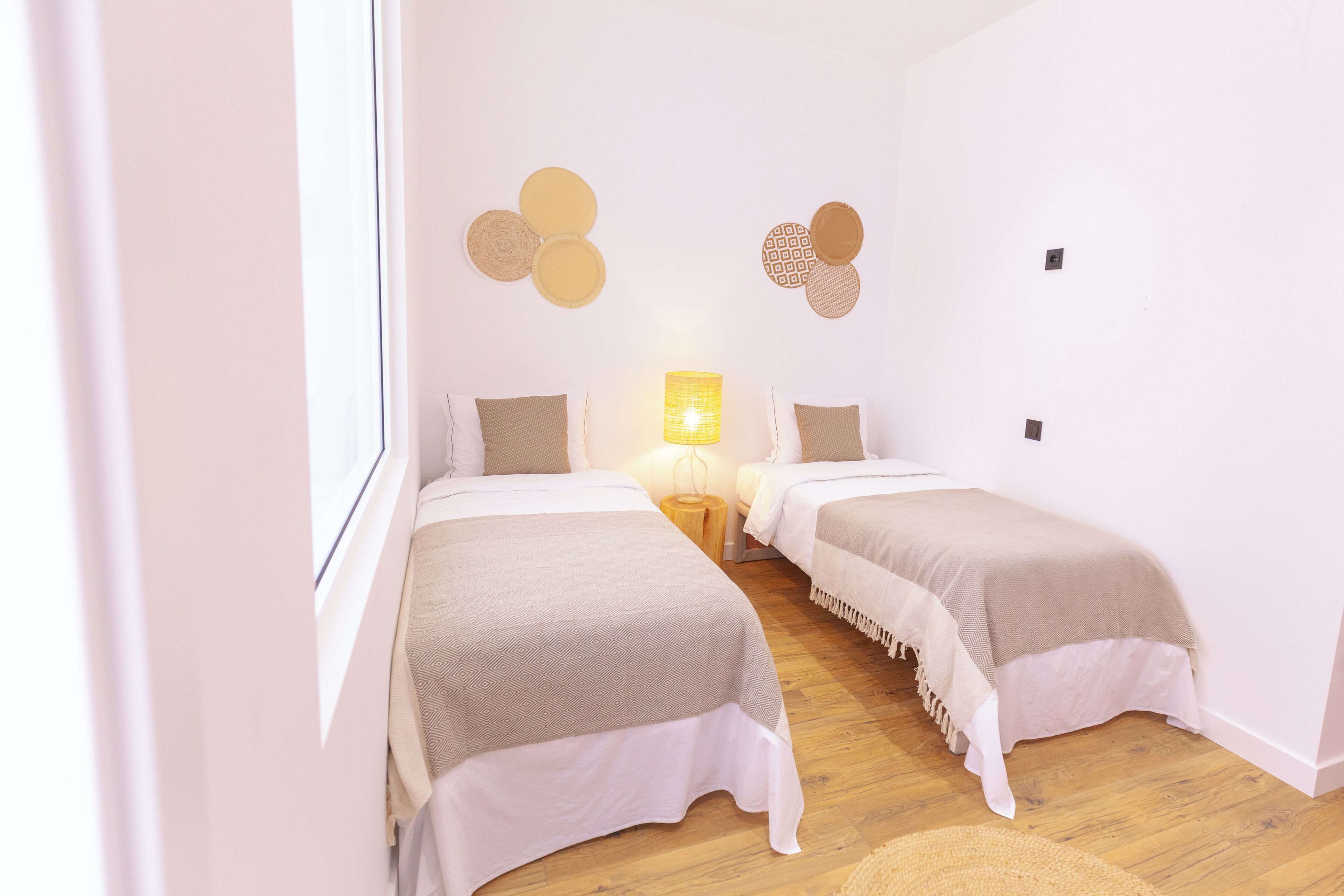 A room with two beds, a small table, a lamp, and wall decor.