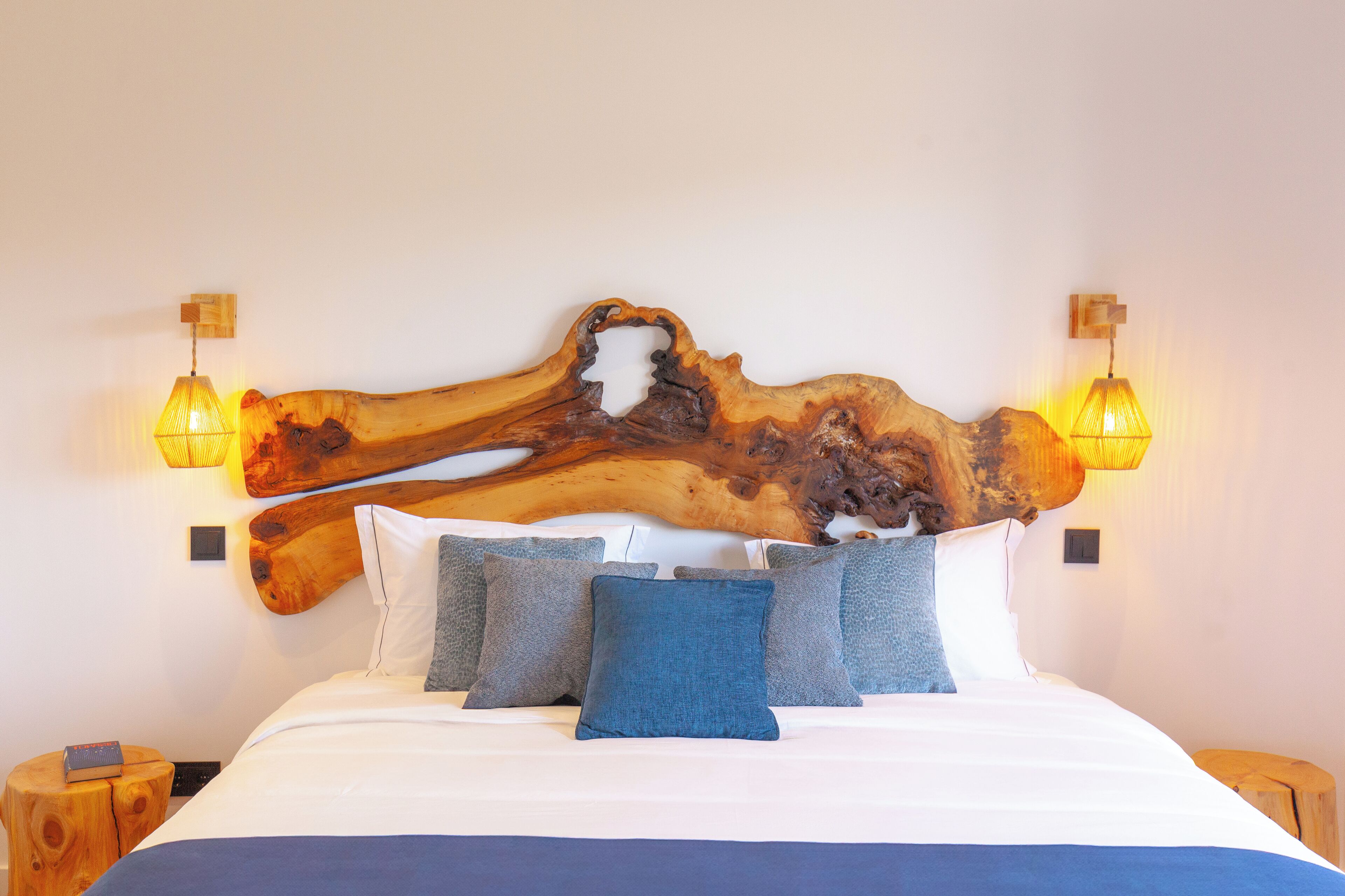 Una cama con una original cabecera de madera, varios almohadones y dos lámparas fijadas a la pared.