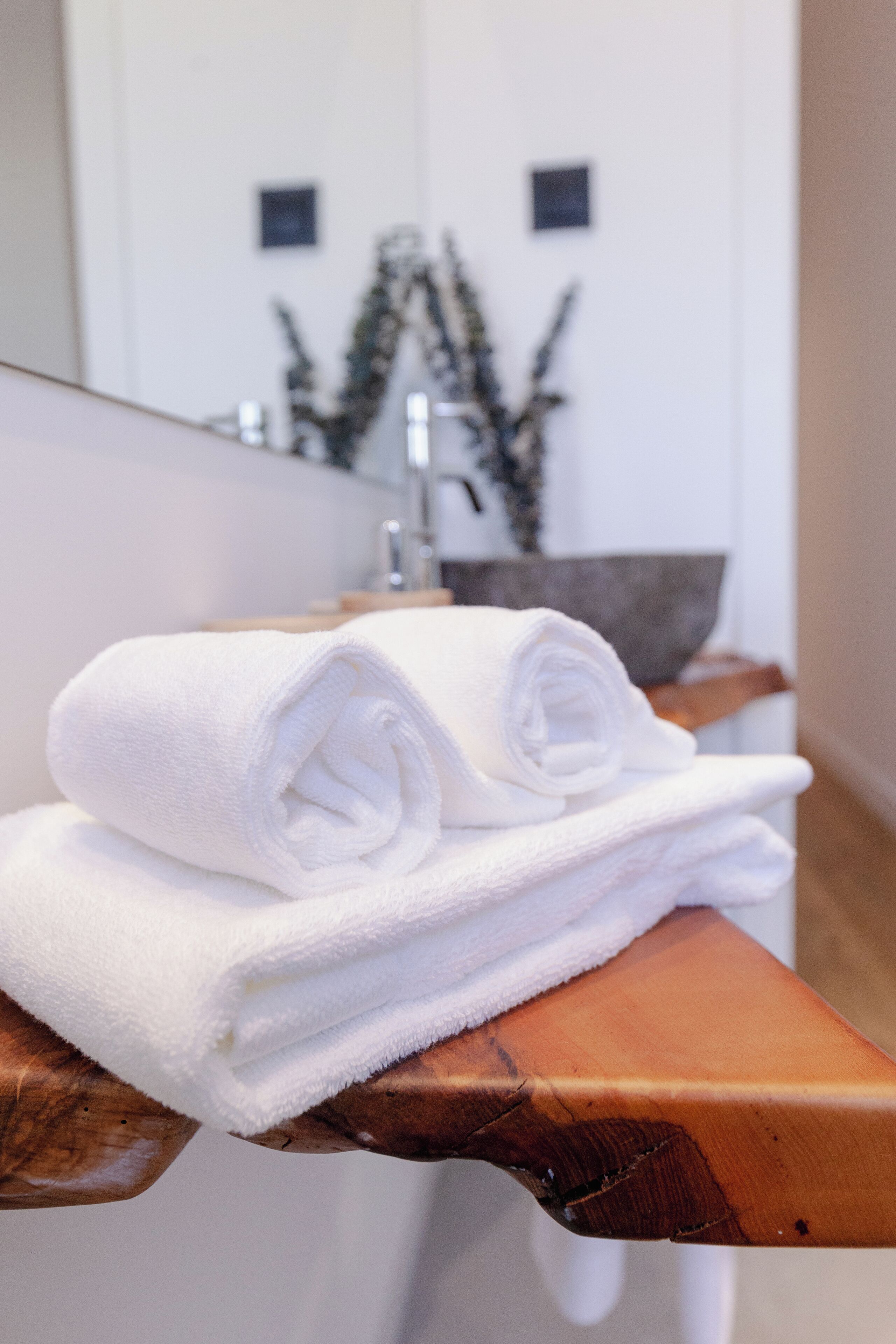 A stack of white towels on a wooden bench in a bathroom.