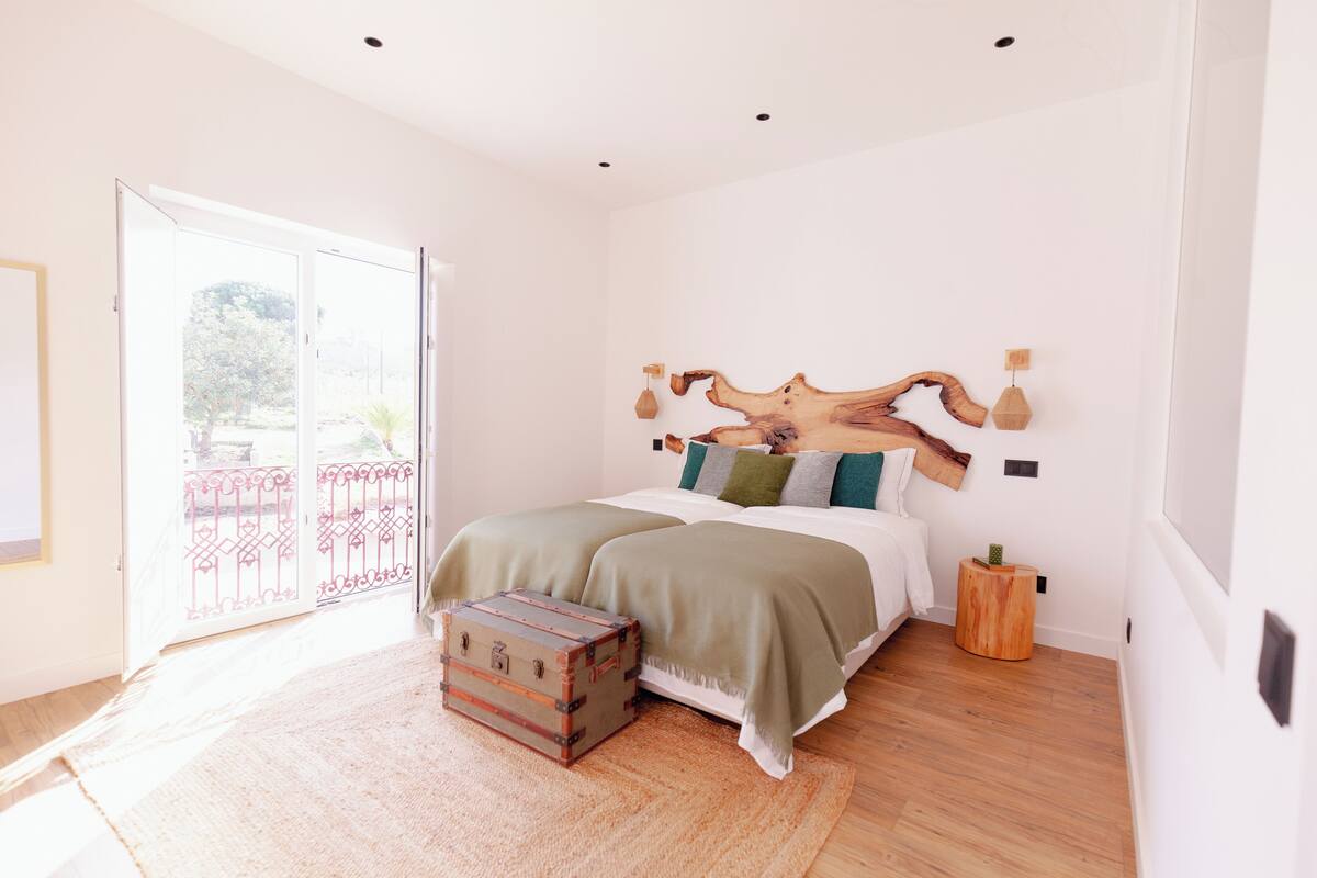 A bedroom with a large bed, a wooden headboard, a suitcase, and a view of a balcony.