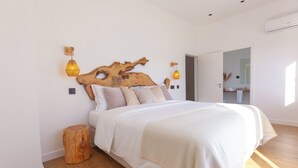 Un dormitorio con cabecera de madera, una cama con ropa blanca, dos lámparas fijadas a la pared y un taburete de madera.