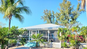 A glass-roofed building with a white exterior, surrounded by tropical vegetation and a paved area with steps leading to the entrance. - Colibri Oasis 3-BR Villa in wonderful Grace Bay with Pool steps from your door! (Grace Bay)