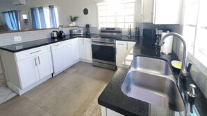 A kitchen with white cabinets, a black countertop, stainless steel appliances, and a window with curtains. - Colibri Oasis 3-BR Villa in wonderful Grace Bay with Pool steps from your door! (Grace Bay)