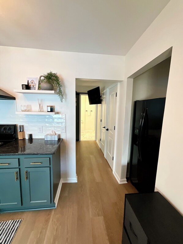 A modern kitchen with teal cabinetry, a black refrigerator, and a flat-screen TV mounted on the wall.