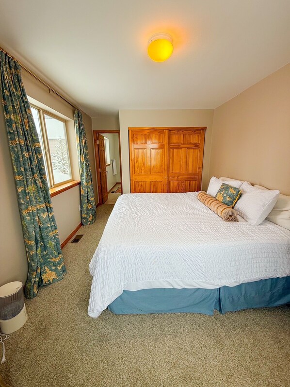 A bedroom with a large bed, wooden wardrobe, and a window with curtains.