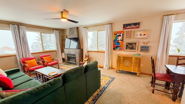 A cozy living room with a green sofa, red chairs, a wooden coffee table, and a fireplace. - 3/3 Townhome in Fraser just steps from the Black line! (Granby)