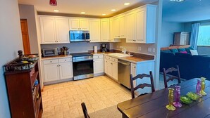 A modern kitchen with white cabinets, a dining area with a wooden table and chairs, and a chandelier. - 3/3 Townhome in Fraser just steps from the Black line! (Granby)