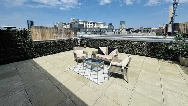 Una terraza en la azotea con mobiliario exterior, vista del paisaje urbano y una grúa de construcción al fondo.