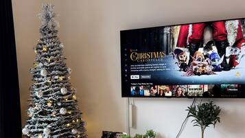 A living room with a Christmas tree, a flat-screen TV, a white entertainment unit, and a potted plant.