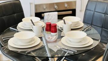 A round glass table with white plates, bowls, and cups, surrounded by black leather chairs.