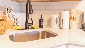 A kitchen with a stainless steel sink, a black faucet, a kettle, and various utensils. - Transit Oasis: EWR 8 Min/Penn with Free Parking (Newark)