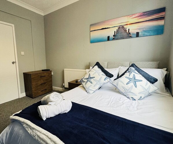 A neatly made bed with star-patterned pillows, a blue throw blanket, and a white towel on the floor.