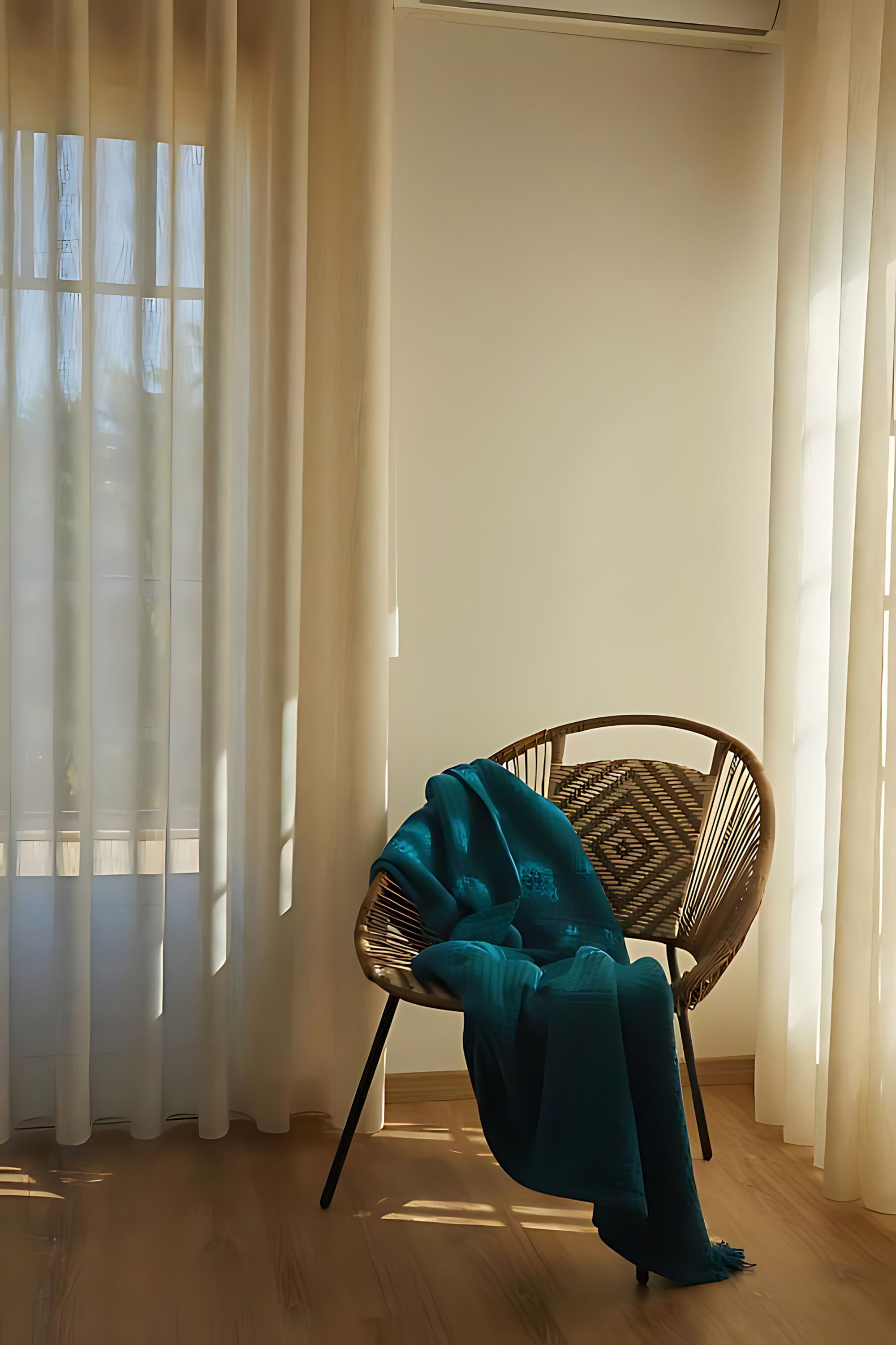 A room with a wooden floor, a wicker chair, and sheer curtains.