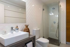 Ein modernes Badezimmer mit einem großen weißen Waschbecken, einem Spiegel, einer Toilette und einer Duschkabine.