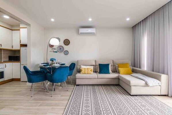 Un salon moderne comprenant un canapé, une table à manger avec des chaises, un coin cuisine et un tapis à motifs.