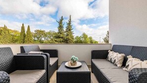 Ein Balkon mit Korbmöbeln, einem kleinen Tisch und einem dekorativen Gegenstand, mit Blick auf Bäume und Himmel.