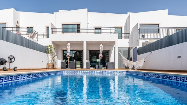 Un edificio moderno con piscina, asientos al aire libre y fachada blanca.