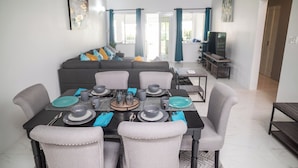 A dining area with a table set for four, surrounded by grey upholstered chairs. - RVR Rentals (Montego Bay)