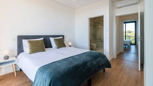 A modern bedroom with a large bed, bedside lamps, a walk-in shower, and a view of the outdoors.