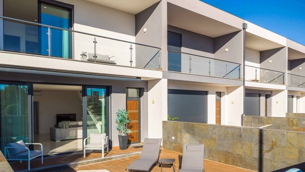A modern multi-story building with a swimming pool, outdoor seating, and a balcony.