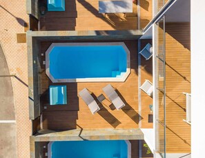 An aerial view of a rooftop swimming pool with two separate pools, wooden decking, and lounge chairs. - Villa Alegre With Private Pool (Albufeira)