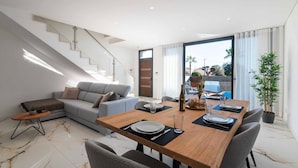 A modern living room with a dining area, a staircase, and a large window with a view of the outside.