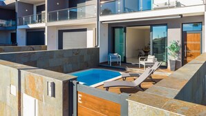 A modern multi-story residential building with a rooftop pool area, outdoor seating, and a glass door entrance.