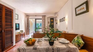Un coin repas avec une table dressée pour deux personnes, une plante en pot et une vue sur l’extérieur.