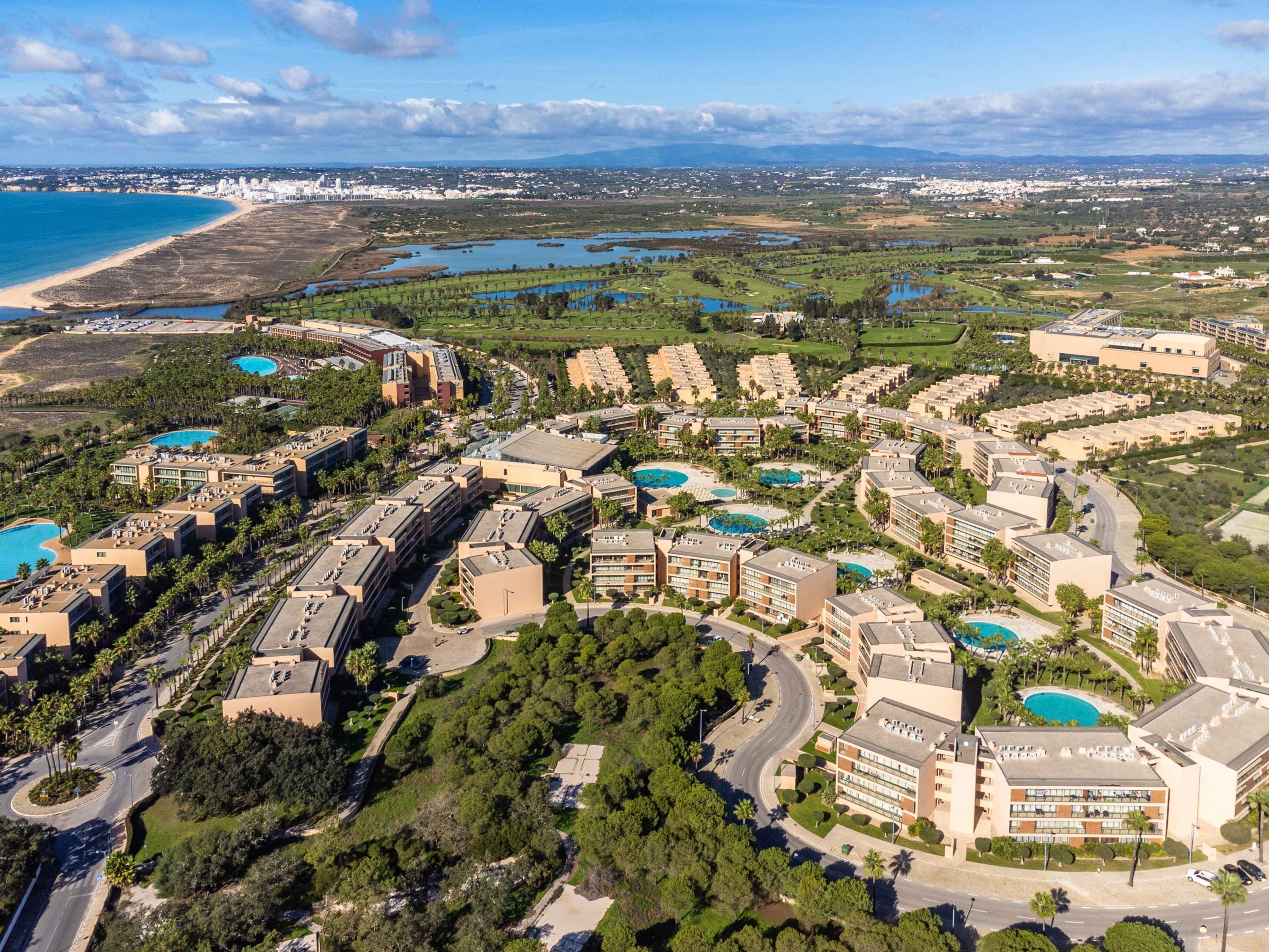 Vista aerea di un resort con diversi edifici, piscine e spiaggia.