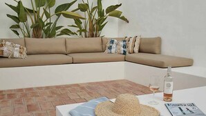 A modern outdoor seating area with a beige sofa, a woven hat, a glass of wine, and a magazine on a table.
