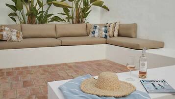 Un espacio exterior moderno con un sofá color beige, un sombrero tejido, una copa de vino y una revista sobre una mesa.