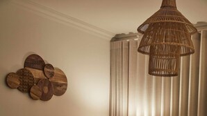 Un salon moderne avec un canapé, un pouf et un fauteuil en osier. On peut également apercevoir une lampe et une œuvre d’art murale.