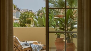 Un balcon donnant sur un quartier résidentiel, agrémenté de deux plantes en pot et d’un espace détente avec une table et des chaises.
