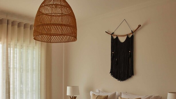 Une chambre avec un lit en bois, deux tables de chevet avec des lampes, un luminaire suspendu en fibres tressées et une décoration murale en macramé.