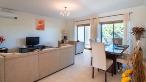 A modern living room with a sofa, TV, and dining area with a table and chairs. - Balaia Residence 2 Bedroom Penthouse With Pool (Albufeira)