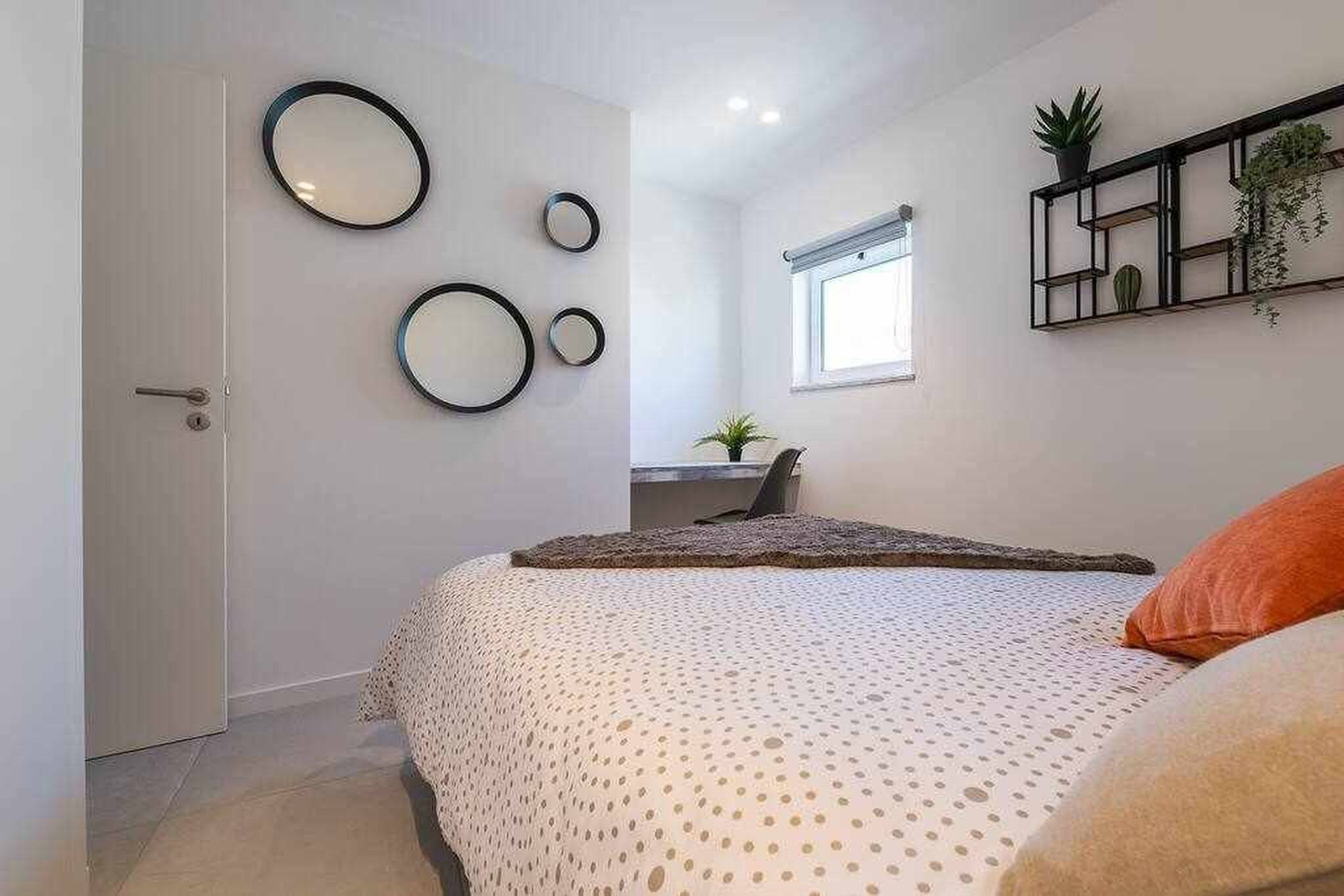 A bedroom with a bed, a desk, and a window.