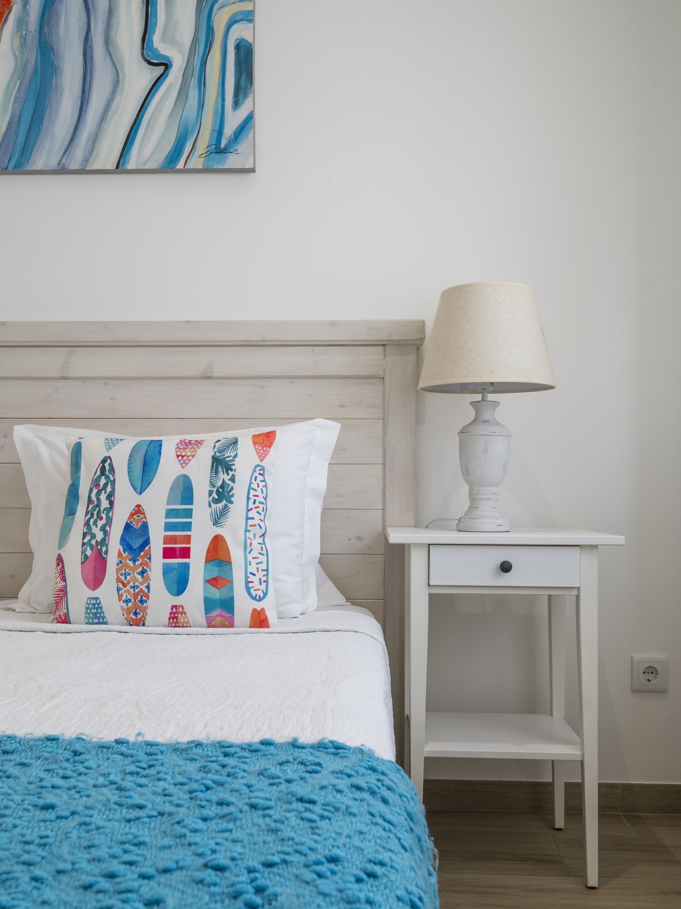A bedroom with a bed, a bedside table with a lamp, and a wall with a painting.