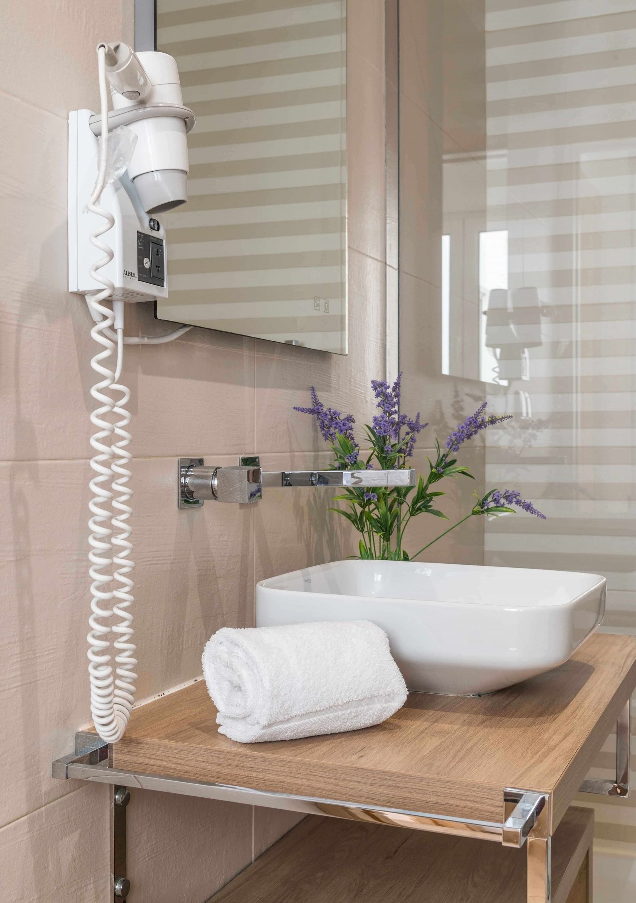 Une salle de bain avec un lavabo blanc, une serviette, un sèche-cheveux et un miroir.
