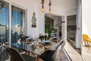 A modern dining area with a glass table, black chairs, and a view of the city. - Salgados Village T2 Apartment - 800m da Praia (Albufeira)