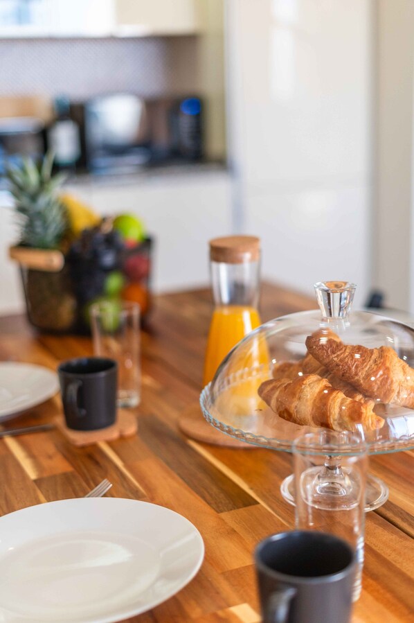 A breakfast setting with croissants on a glass stand, a glass of orange juice, and a fruit bowl in the background.