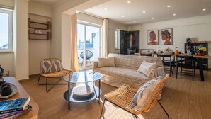 A modern living room with a sofa, two chairs, a glass coffee table, and a dining area with a table and chairs. - Montechoro Sea View 3 Bedroom Apartment (Albufeira)