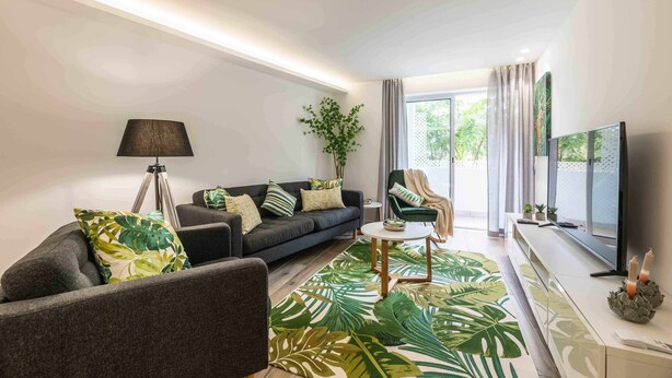 Ein modernes Wohnzimmer mit einer Couch, einem Sessel und einem Couchtisch. Ein Fernseher auf einem Schrank, eine Lampe und eine Pflanze sind ebenfalls vorhanden.