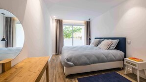 Ein modernes Schlafzimmer mit einem großen Bett, einem Nachttisch, einem Spiegel und Blick ins Freie.