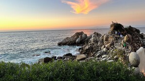 Paesaggio costiero roccioso con vista al tramonto, caratterizzato da una scala in pietra che conduce a una terrazza panoramica.