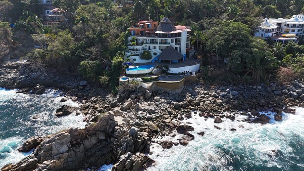 Una proprietà costiera con una grande casa, diversi balconi, una piscina e un litorale roccioso.