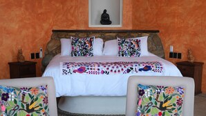 Una camera d'albergo con un letto, due poltrone, un tavolino e una ventola a soffitto.